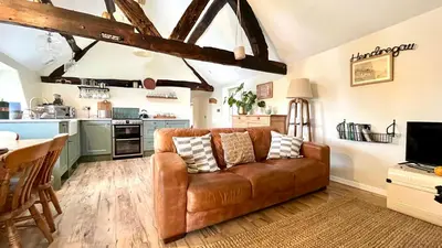 a living room with a brown couch and a kitchen at Peaceful Dyfi Valley Cottage - Hendre-gau in Machynlleth