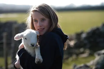 a young woman holding a baby lamb in her arms at Gegin-Faeldre in Llanbedr