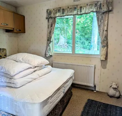 an unmade bed in a room with a window at Family-Friendly Woodland Caravan Pool & Bar in Bryn-glâs Station