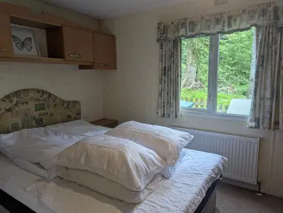 a bedroom with a bed with white sheets and a window at Family-Friendly Woodland Caravan Pool & Bar in Bryn-glâs Station