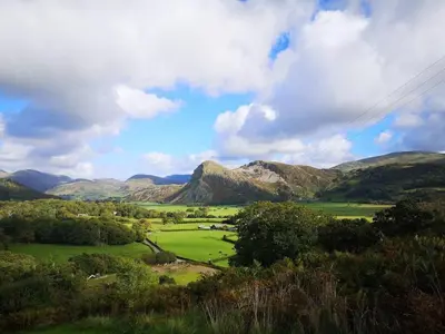 a view of a green field with mountains in the background at Family-Friendly Woodland Caravan Pool & Bar in Bryn-glâs Station
