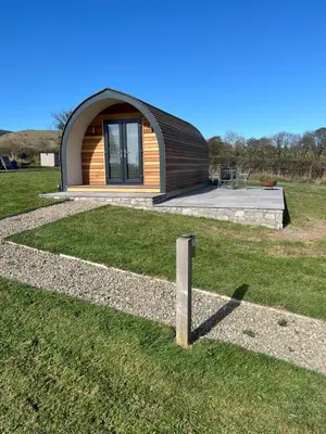 a small house in a grassy field with a building at Mynd View Pods Cedar in Craven Arms
