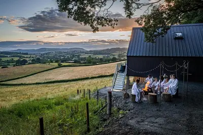 a group of people sitting around a fire in front of a barn at Oolert Treehouse in Hundred House