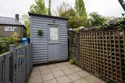 a small blue shed with a stone fence at Cosy townhouse with log burner in Dolgellau