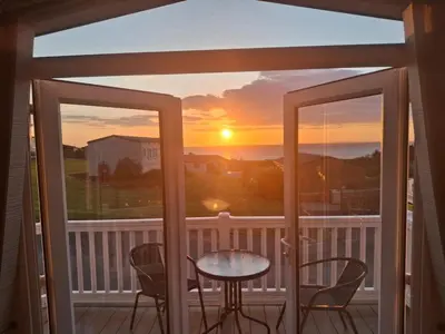 a balcony with a table and chairs and a sunset at 'Falcons Rest' in Borth