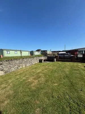 a grassy field with a stone wall and a building at Y Caban Caru in Tywyn