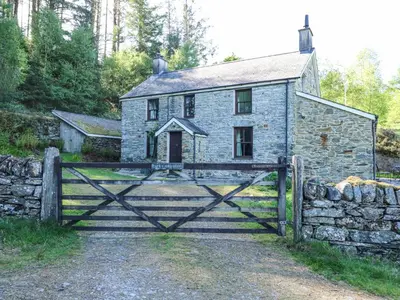 an old stone house with a gate and a stone wall at Cae'n Y Coed Cottage in Talsarnau