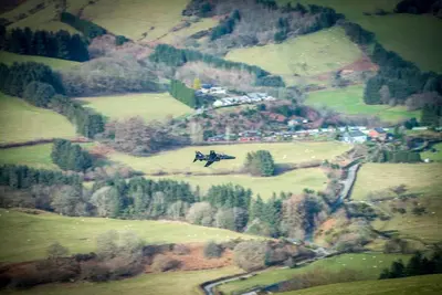 a plane flying over a field in a mountain at Beudy-Mach in Cemmaes Road