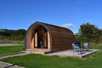 a small wooden cabin with two chairs and a grill at Mynd View Pods Ash in Craven Arms