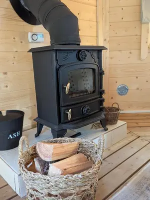 a black stove sitting in a room with a basket at Bluebell Hideaway in Llanfair Clydogau
