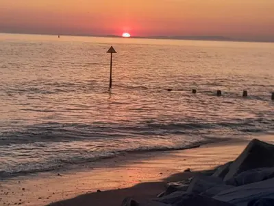a sunset over the ocean with a pole in the water at 254 Bryn y Mor in Tywyn