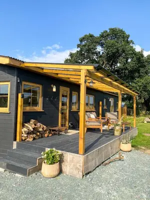 a black tiny house with a wooden deck at The Meadow Snug in Baschurch