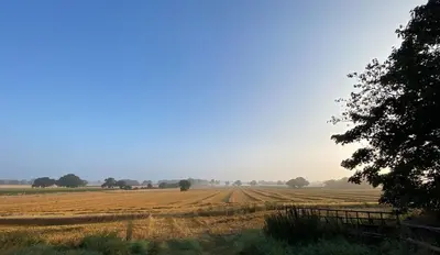 a field of hay with a fence in the foreground at The Meadow Snug in Baschurch
