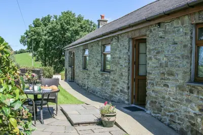 a stone house with a table and a patio at Y Dderwen Aberaeron in Llanarth