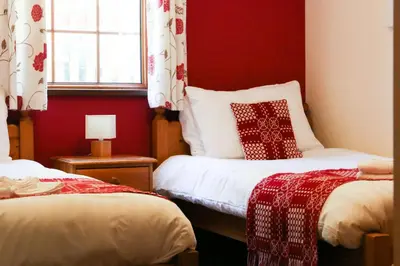 a room with two beds with red walls and a window at Yr Onnen Aberaeron in Llanarth