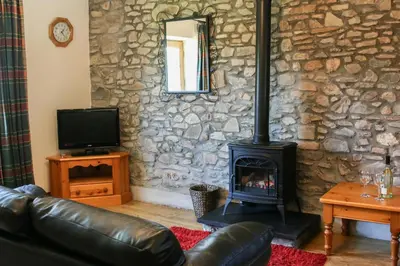 a living room with a stone wall with a fireplace at Yr Onnen Aberaeron in Llanarth