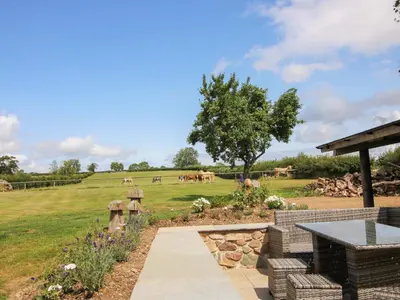 a garden with a table and a field with horses in the background at The Long House in Oswestry