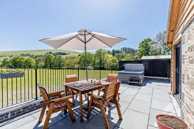 a patio with a table with an umbrella and a grill at 2 Bed in Llanarmon Dyffryn Ceiriog oc-b31110 in Llanarmon Dyffryn-Ceiriog