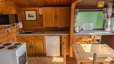 a kitchen with wooden cabinets and a table in a cabin at Happy Place LogCabin in Trawsfynydd
