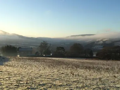 a field with a fog in the distance with a house and mountains at The Royston in Llanbrynmair