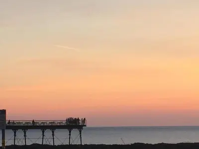 a group of people standing on a pier at sunset at Awel Mor 3 Luxury Apartment in Aberystwyth