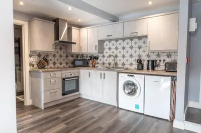 a kitchen with white cabinets and a washer and dryer at Mermaids Hideaway in Aberaeron