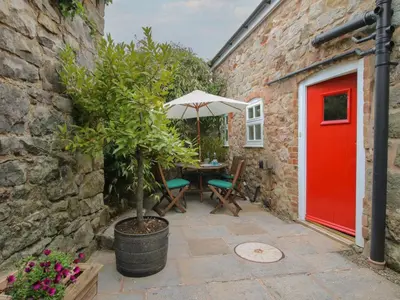 a patio with a red door and a table with an umbrella at Little Barn in Oswestry