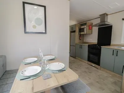 a kitchen with a wooden table with plates and glasses at 8 Puffin Way in Llwyngwril