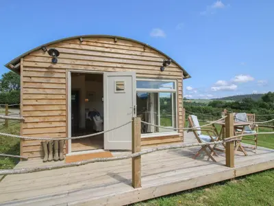 a small wooden cabin with a deck and a chair at Owl's Hollow in Bucknell