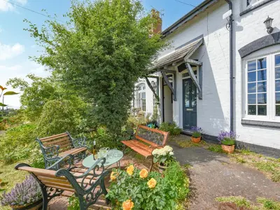 two benches and a table in front of a house at Clee View Cottage in Ludlow
