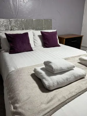 a large white bed with purple pillows and towels on it at Vesna Affordable comfort in Newtown