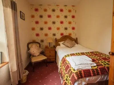 a small bedroom with a bed and a chair at Ty Ffarm, Gogarth