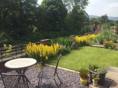 a garden with a table and chairs and flowers at Outstanding Llangollen Riverside Apartment in Llangollen
