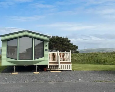 a green house with a porch sitting on display at Sanderling, 289 Ynyslas Beach, Borth in Borth