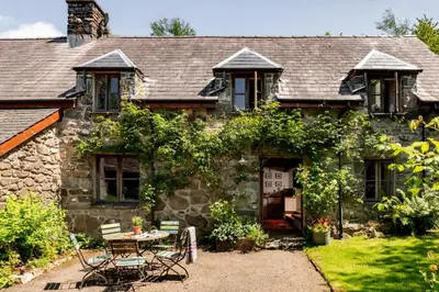 an old stone house with a table and chairs at Gwanas Fawr in Dolgellau