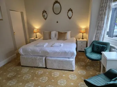 a bedroom with a large bed and a green chair at Caer Beris Hotel in Builth Wells