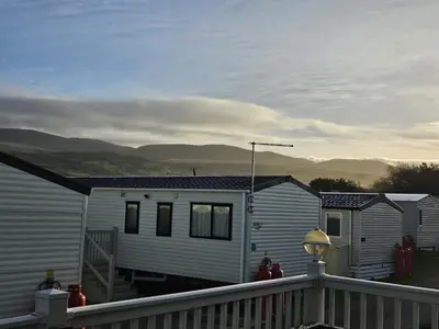 a small white house with mountains in the background at 186 Barmouth Bay Holiday Park in Barmouth
