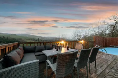 a deck with a couch and a table and chairs at Cae Madog Barn in Llanbrynmair