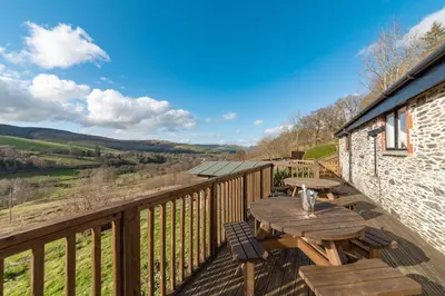 a wooden deck with a wooden table and chairs at Cae Madog Barn in Llanbrynmair