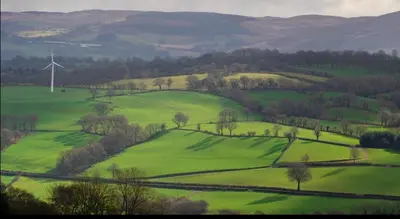 a green field with a wind turbine in the distance at Pencastell Views in Nantcwnlle