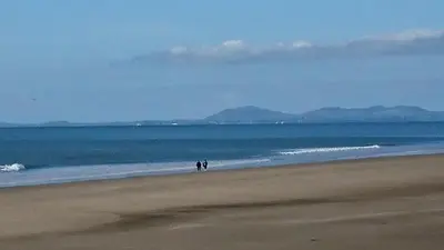 two people walking on a beach near the ocean at Cadwgan Caravan No2 in Barmouth