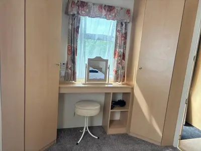 a dressing table with a mirror and a stool under a window at Cadwgan Caravan No2 in Barmouth