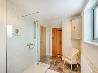 a glass shower in a bathroom with a chair at Orchard Barn in Llandrindod Wells