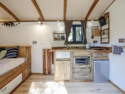 a kitchen with wooden cabinets and a bed in a room at Tanglewood Shepherds Hut in Welshpool