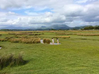 two girls walking across a field with a river at Large farmhouse in Snowdonia, North Wales in Talsarnau