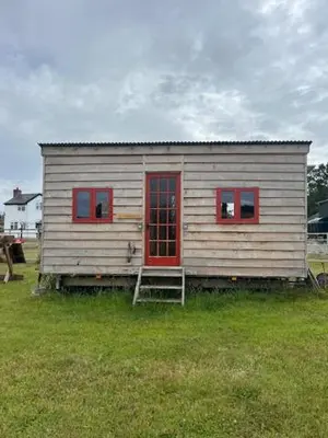 a small house with red windows and a ladder at Black Bridge Cabin in Lyonshall