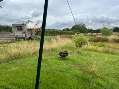 a grill in the middle of a field with a house at Tick Bridge cabin in Lyonshall