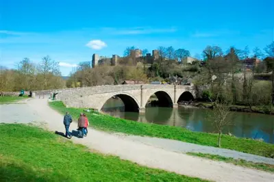 two people walking down a path next to a bridge at Ludford View, riverside cottage in Ludlow with private parking in Ludlow