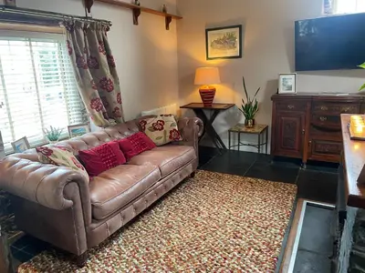 a brown leather couch in a living room with a television at Y Bwthyn in Llanfihangel-geneuʼr-glyn