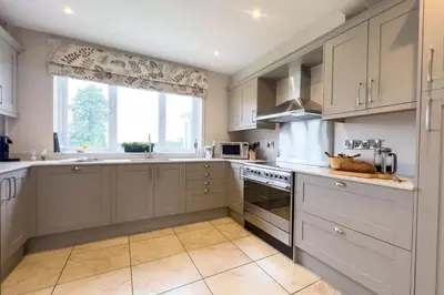 a kitchen with white cabinets and a large window at Wellingtonia Cottage in Chirbury